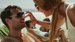 Young woman applying sunscreen to mans nose on beach Stock Footage