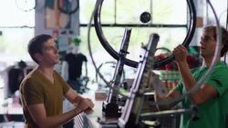 Bike shop mechanic takes bicycle wheel from customer, places on truing stand, and spins Stock Footage