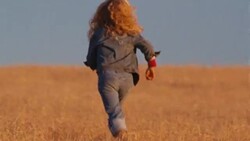 Little girl with blonde hair runs away from camera in a field of golden prairie grass. Stock Footage