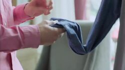 Young holds up shirtsleeve to read price tag in modern clothing store Stock Footage