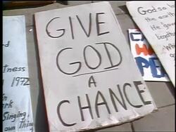 1972 tilt up from close up of "Give God a Chance" poster to male hippie lying on sidewalk Stock Footage