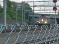 Commuter train slowly passing the camera.  Shot begins with out-of-focus chainlink fence with train approaching and then camera focuses on train as it passes. Stock Footage