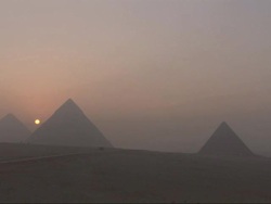 Wide Shot, static  - An orange sun glows through the smog between the Great Pyramids of Giza / Egypt Stock Footage