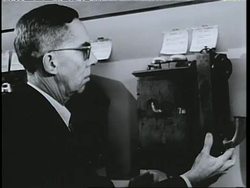 A man cranks an early telephone before he can talk; a woman talks into a telephone with a shoulder rest. News Clip