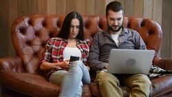 young couple sitting on sofa and using gadgets Stock Footage