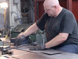 workman wearing protective gloves punches out precut holes in piece of sheet metal / Redlands, California, USA Stock Footage