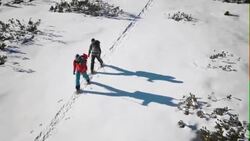 Aerial of winter mountaineers snowshoeing across valley on sunny day Stock Footage