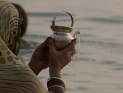 MS CU ZI Woman pouring water from small pot in river and praying / India Stock Footage