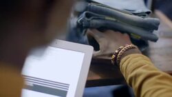 Modern shop worker checks tags on jeans and enters info on tablet in clothing store Stock Footage