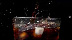 Pouring cola soda into glass of ice with splashes at slow motion on a black background Stock Footage