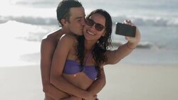 Young couple taking self-portraits with camera phone at beach Stock Footage