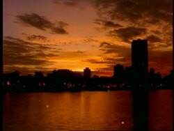 T/L WA view across river to city skyline, against dramatic orange dusk sky, reflected in water, darkening, Singapore Stock Footage