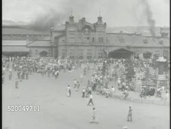 1950: SOUTH KOREA: HA WS Crowded train station, Koreans gathered on streets. WS Stationary cargo train carrying various military vehicles, including jeeps & wagons (L) frame, Korean children walking on railroad tracks (R) frame. Korean War Instructional Video