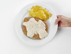 CU Woman hand entering setting down round white plate with chicken fried steak, gravy and breakfast hash browns / Omaha, Nebraska, United States Stock Footage