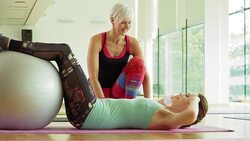 Personal trainer guiding woman doing sit-ups with fitness ball in gym Stock Footage
