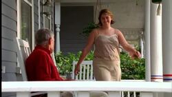 A woman joins an elderly man sitting in a rocking chair on a porch decorated with American flags. Stock Footage