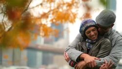 Young man in love wraps arms around and kisses girlfriend in park, autumn leaves in foreground (dolly-shot) Stock Footage