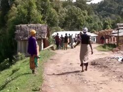 MS Shot of  woman walking on dirt road with people and houses in distance / bwindi, kabale, uganda Stock Footage