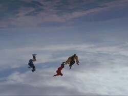 Two skydivers perform a rodeo dive with one on top of the others back.  Another skydiver and camera flyer fly around them. Stock Footage
