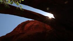 Looking up at the blue sky and sun through a red-rock mountain arch in the desert in Utah Stock Footage