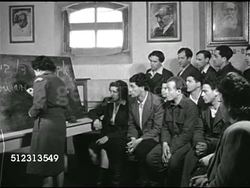 1946: POST-WAR EDUCATION: WS People & children walking in yard of Displaced Persons' Camp. American Joint Distribution Committee (AJDC) volunteer teaching English using blackboard. MS Young adults working on papers at table. Instructional Video