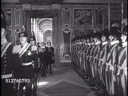 1940: VATICAN: THE ROMAN CURIA: The Swiss Guard standing at attention as visitors in uniform walk down hallway. Cardinal Secretary of State the Roman Curia Luigi Maglione (1877-1944) seated at desk, looking over paperwork, talking (No SOT). Instructional Video