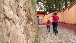 Hispanic teenage brother chases younger children up third-world street (dolly-shot) Stock Footage