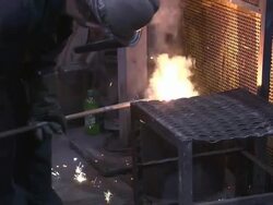 Medium Close Up pan-right tilt-down zoom-in - A foundry worker uses a ladle to pour molten metal into molds /  Ohio, United States Stock Footage