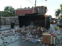 Medium Shot Pan Left - Garbage truck pushing trash down a street / New Orleans Louisiana Stock Footage