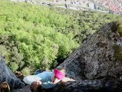 View past belayer's hands to woman climbing rock face Stock Footage