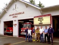 Wide shot group of firefighters standing in front of fire station w/fire engines and flashing sign in background Stock Footage