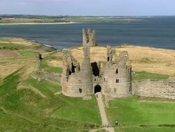 Aerial over ruins of Dunstanburgh Castle on coast of Northumberland / Craster, England Stock Footage