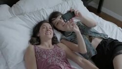 Young women fall back onto hotel bed and laugh at photos on smartphone Stock Footage