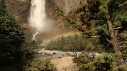 Slide left of a mountain waterfall creating a rainbow over a stream Stock Footage