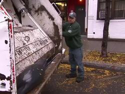 A trash collector places curbside trash into a garbage truck which compacts the contents. Stock Footage