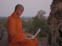 CU, PAN A Buddhist monk types on a laptop computer on top of an ancient temple in Angkor Wat / Siem Reap, Cambodia Stock Footage