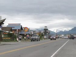 "Businesses on left of Homer Spit Road with lighthouse of The Salty Dawg Saloon central,snow capped mountains of Kachemak Bay State Park and Wilderness Park visible, Home, Kenai Peninsula, Alaska" Stock Footage