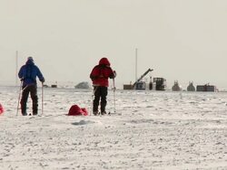 WS View of two people on skis pulling pack sleds across South Pole ice / South Pole, Antarctica Vehicles and storage units in background / South Pole, Antarctica Stock Footage