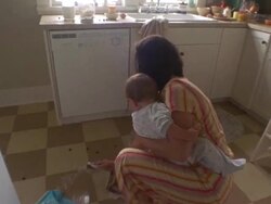MS Mother helping son clean spilled cereal on kitchen floor while holding baby / Washington State, USA Stock Footage