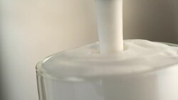 Milk stream falling into glass full of frothy milk Stock Footage