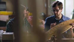 Craftsman shows off elegant design of longboard to worker in wood shop Stock Footage