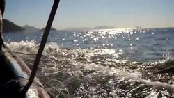 Camera pans with fishing net as it unfurls into the sea from fisherman's hands in slow motion Stock Footage