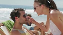 Young woman applying sunscreen to mans nose on beach Stock Footage