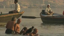 Boaters paddle past bathers near a shore in India. Stock Footage