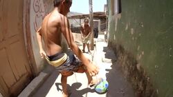 Brazilian street kids dribble soccer ball through stone alley, smile and make peace signs at camera Stock Footage