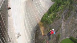 BASE jumper descends from high concrete dam to valley below Stock Footage