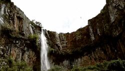 Man traverses highline stretched above waterfall, valley Stock Footage