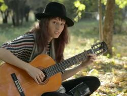 Young woman wearing black hat, playing guitar in park, summer. Stock Footage