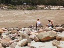 Two senior men sitting at riverbank, Ganges River, Rishikesh, Uttarakhand, India Stock Footage