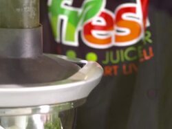 CU TD juice bar employee feeds raw carrots into juicer and applies pressure with food pusher tool as carrots juice flows out of spigot into container Stock Footage